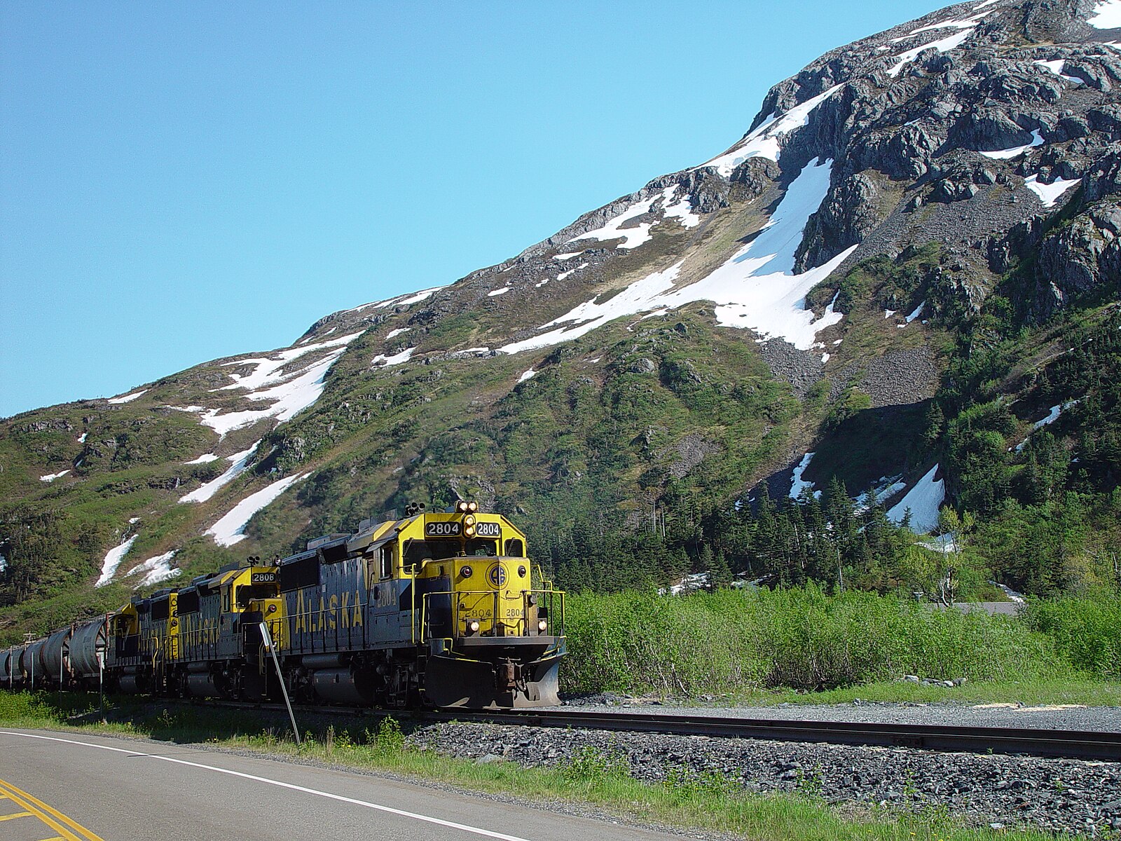 Yellow and blue Alaska Railroad locomotives on the line near Whittier under a clear blue sky