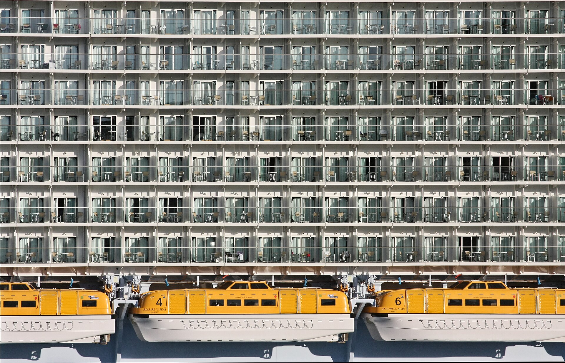 Rows of stateroom balconies above bright yellow lifeboats on the side of Allure of the Seas