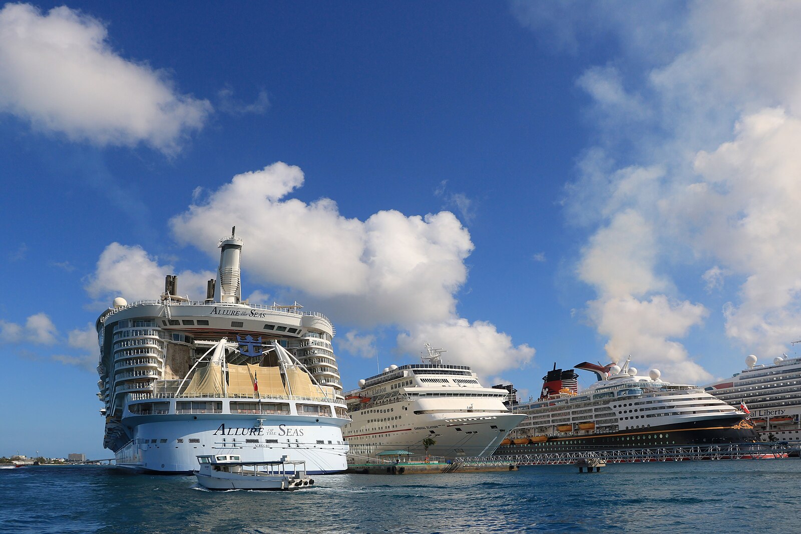 Allure of the Seas moored alongside Carnival and Disney cruise ships under a bright blue sky in Nassau