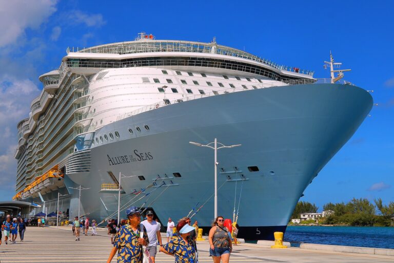 Allure of the Seas docked in Nassau under a bright blue sky, with passengers walking along the pier