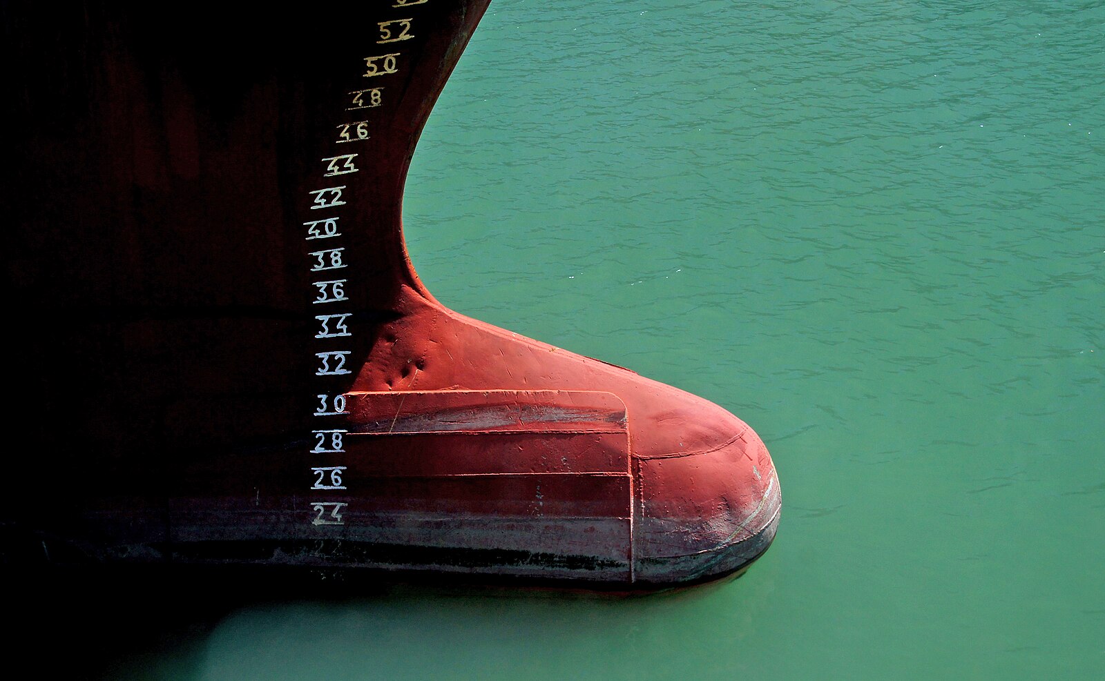 A red bulbous bow protruding forward at the waterline of a ship, against green water