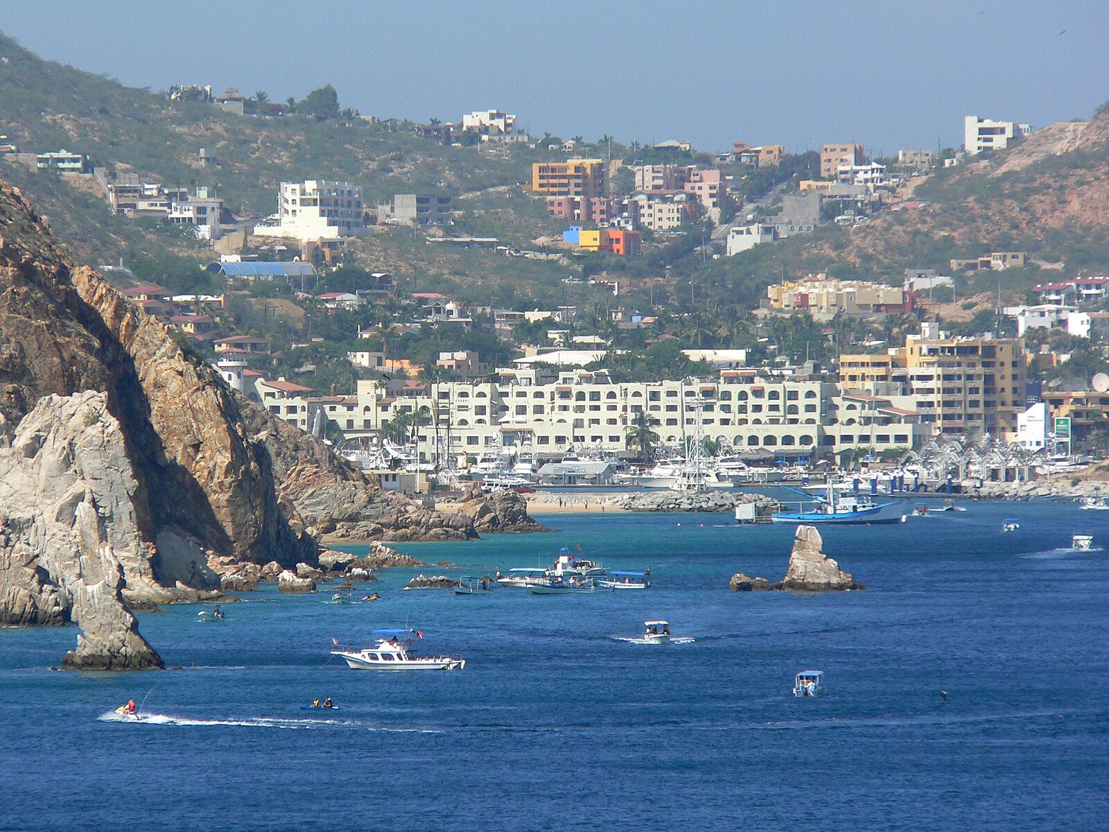 Blue bay of Cabo San Lucas with boats, rock formations and hillside hotels, seen from a cruise ship