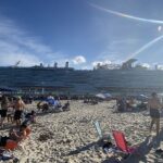Carnival Celebration sailing out of Miami past a sunny beach crowded with people under a blue sky