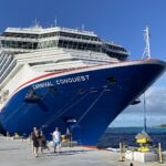 Carnival Conquest docked at Celebration Key in the Bahamas under a bright blue sky, passengers walking on the pier