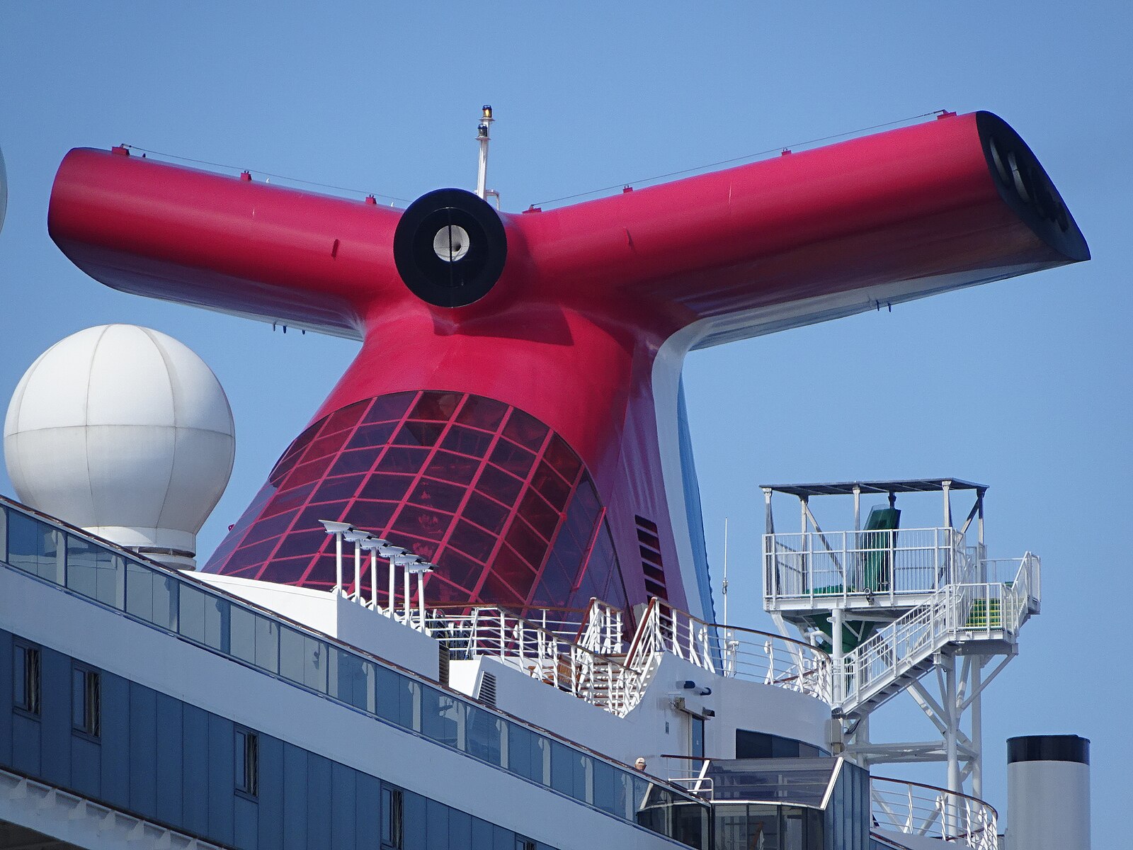 Red Carnival funnel beside a large white satellite radome against a deep blue sky