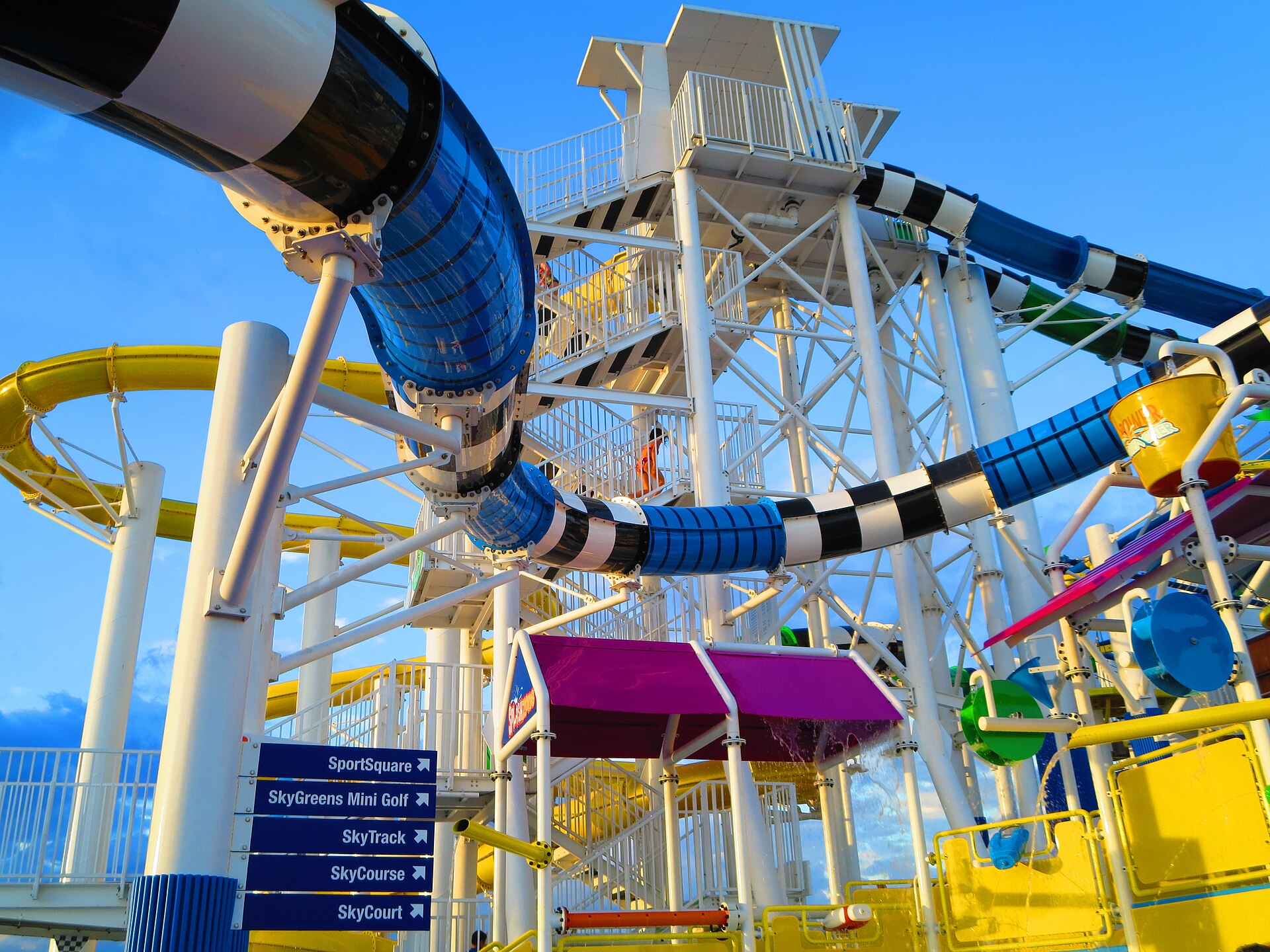 Brightly colored yellow, blue and magenta WaterWorks water slides on the top deck of Carnival Sunshine against a blue sky