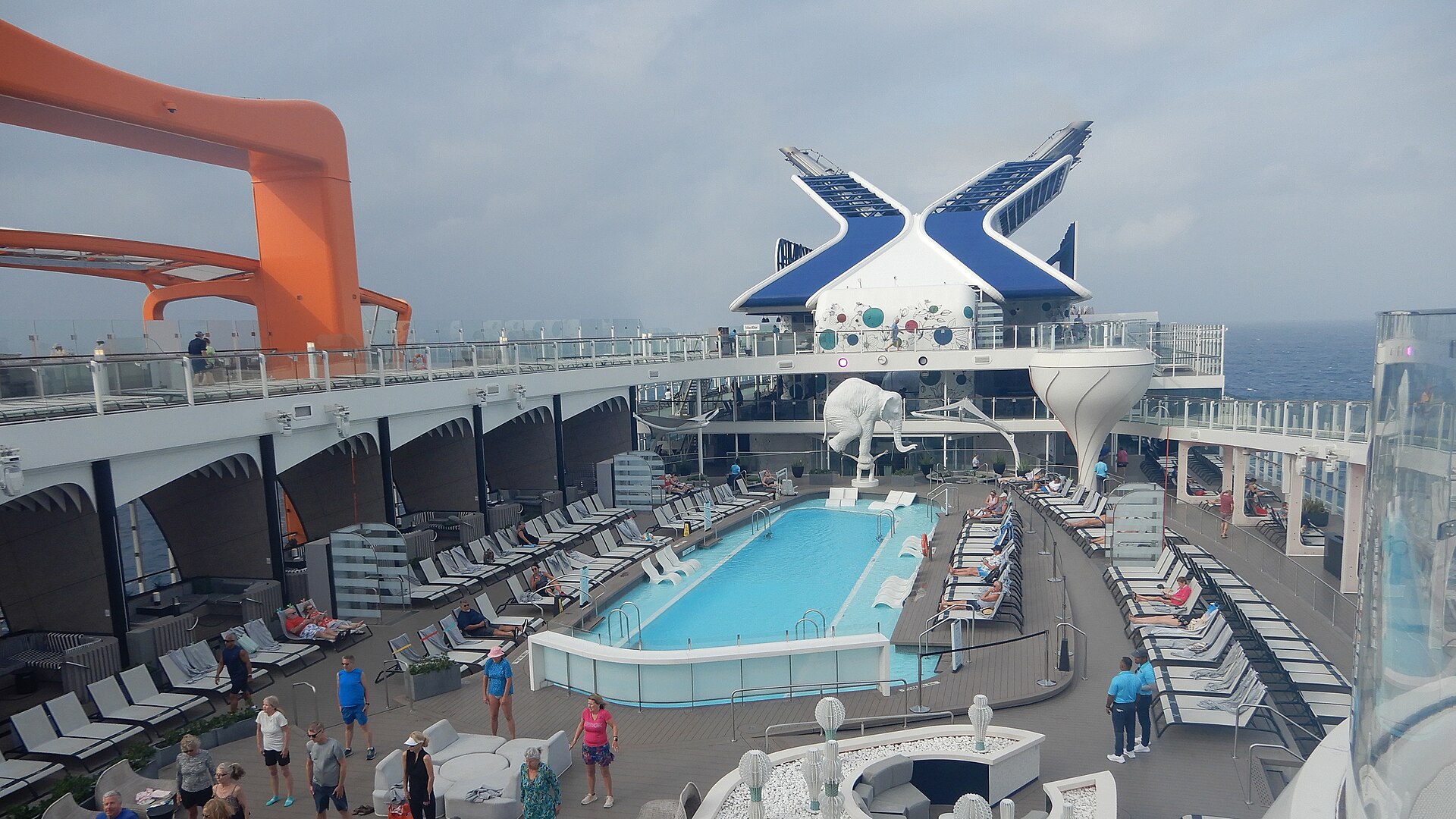 Blue pool and sun loungers on the pool deck of Celebrity Beyond with the orange Magic Carpet platform