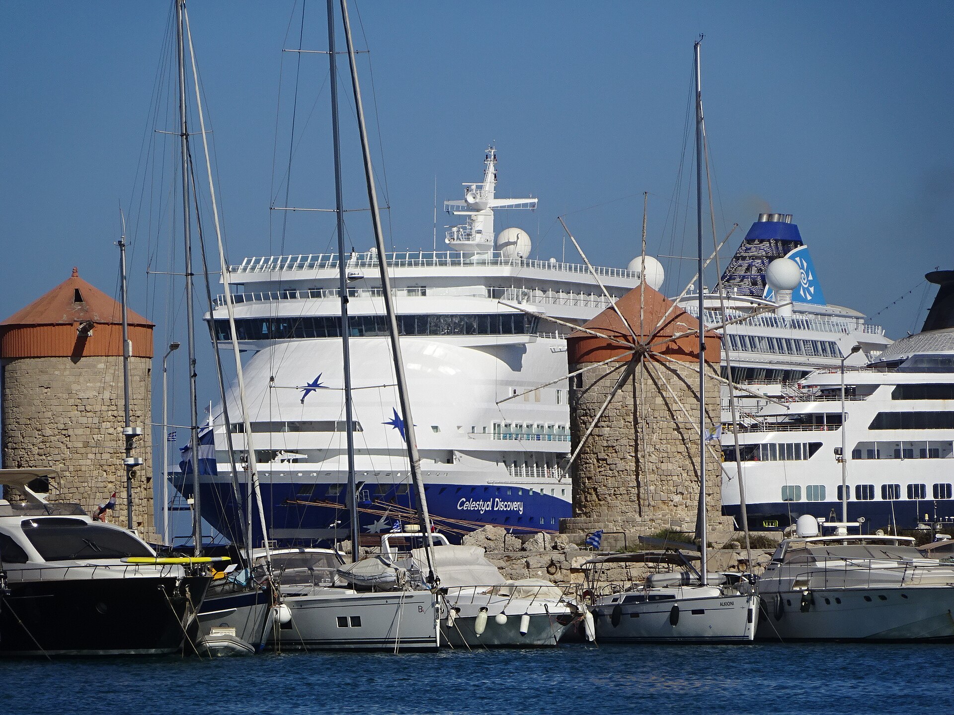 Celestyal Discovery moored in Rhodes behind yacht masts and the old harbour windmills