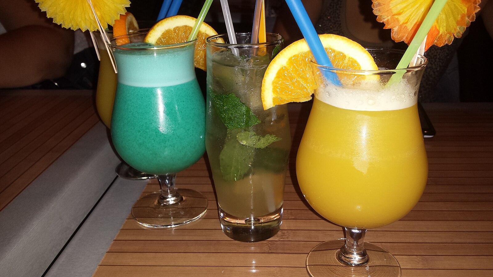 Three brightly colored holiday cocktails in blue, green and orange with fruit garnishes