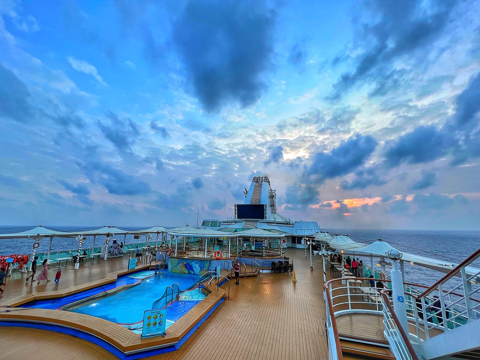 Cruise ship pool deck at sunrise with a vivid blue sky, gold clouds and a turquoise pool