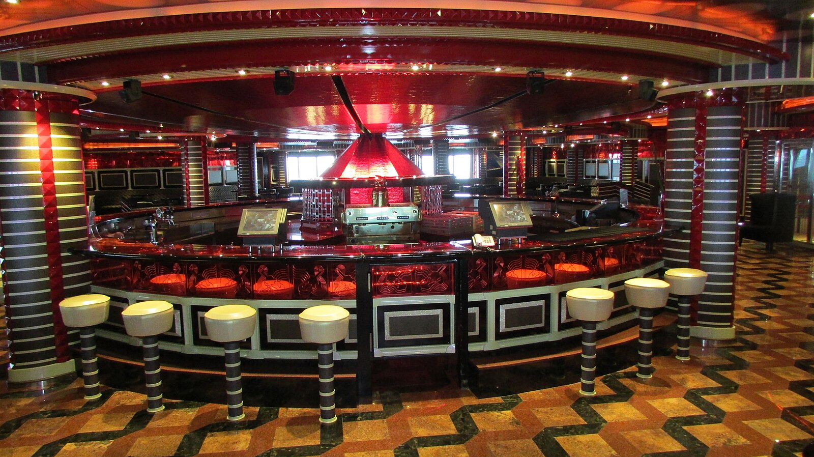 Brightly lit red and chrome cruise ship bar with orange and cream stools