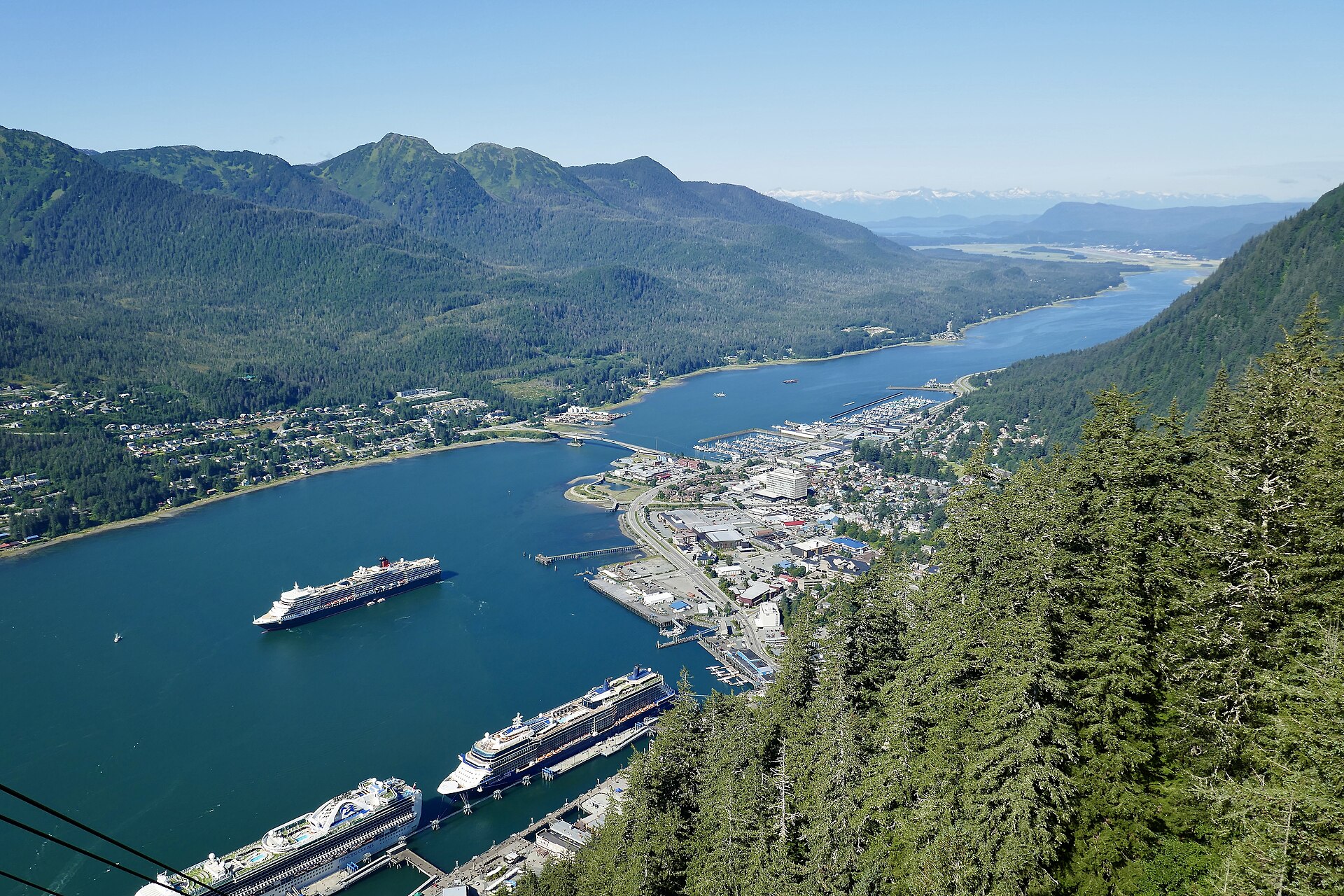 Four cruise ships in Juneau, Alaska, on a sunny day with deep blue water and green forested mountains