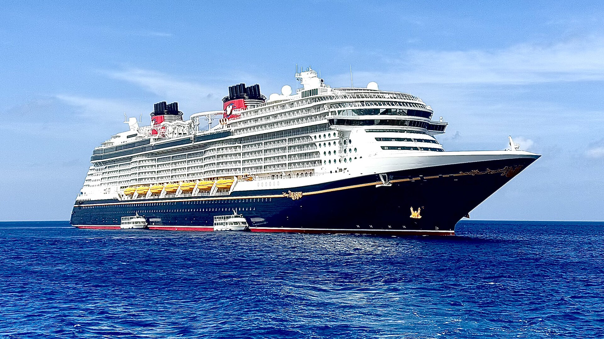 Disney Treasure cruise ship with red and black funnels anchored in deep blue water off Grand Cayman
