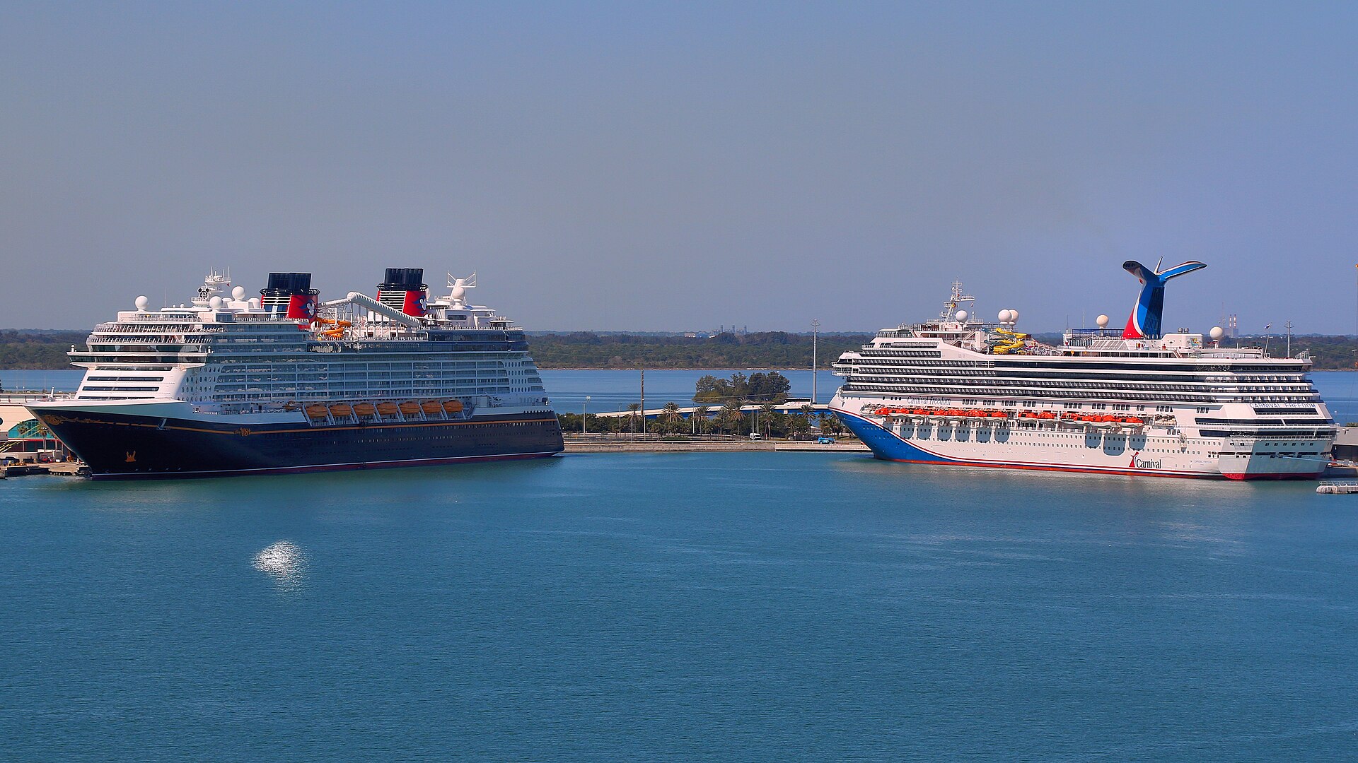 Disney Wish and Carnival Freedom cruise ships docked at Port Canaveral, Florida under a blue sky