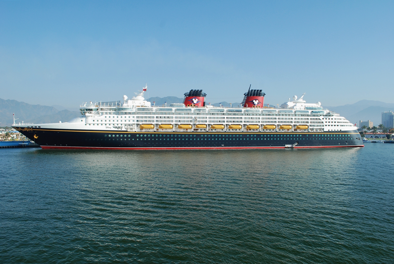 Disney Wonder cruise ship with navy hull and red Mickey funnels docked at Puerto Vallarta under a clear blue sky
