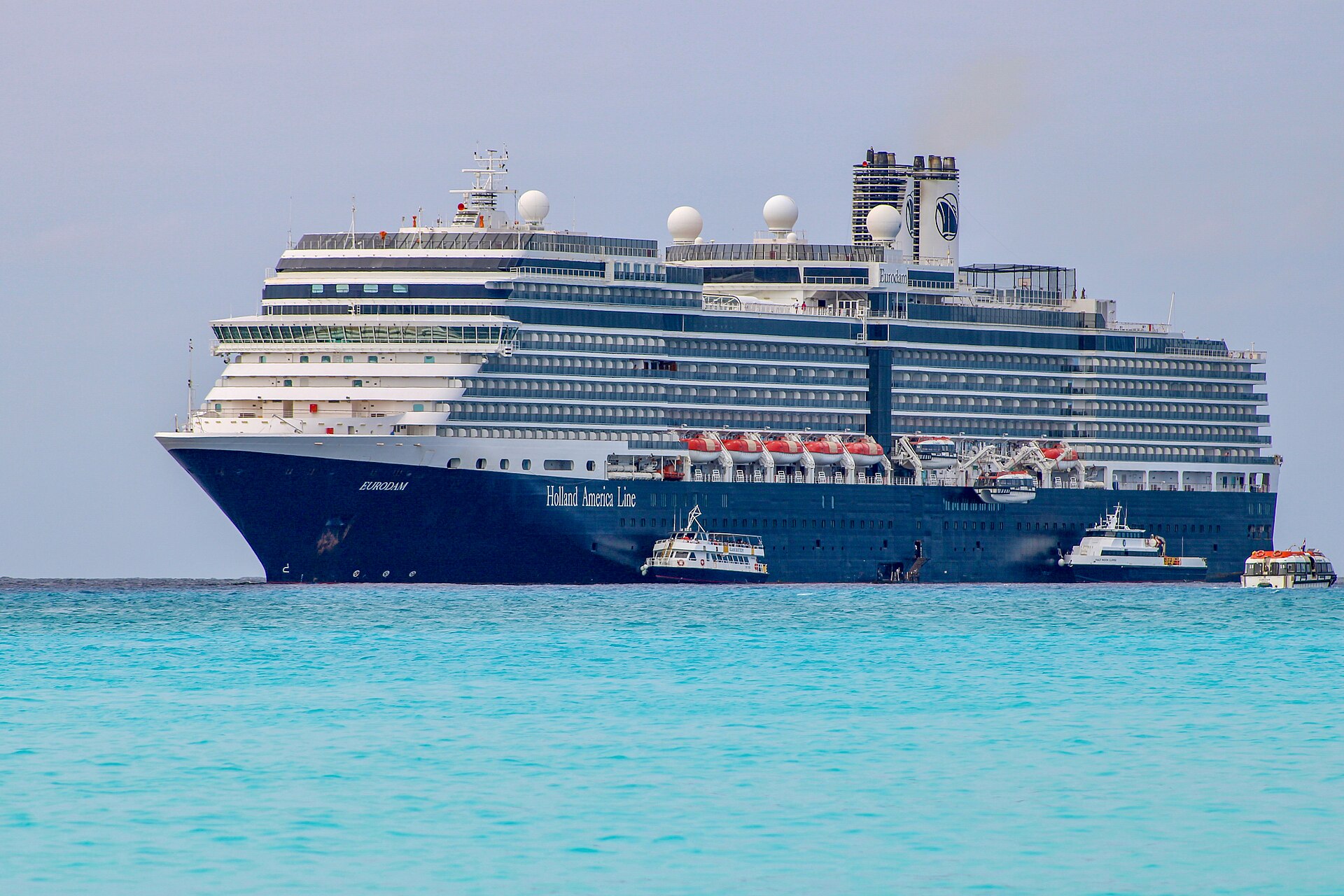 Holland America Line's Eurodam cruise ship with a navy blue hull anchored in turquoise water off Half Moon Cay, Bahamas
