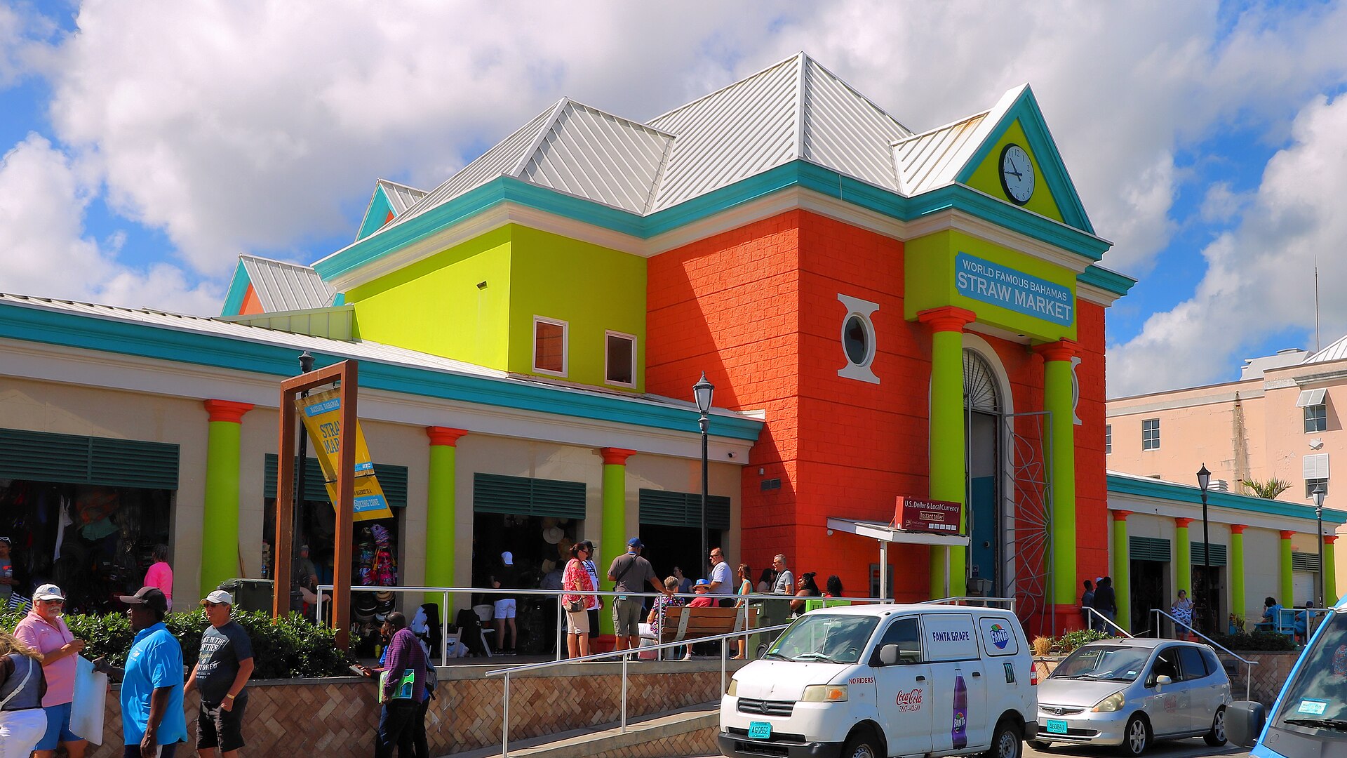 The orange, lime green and turquoise Straw Market building in Nassau, Bahamas, with shoppers outside under a blue sky