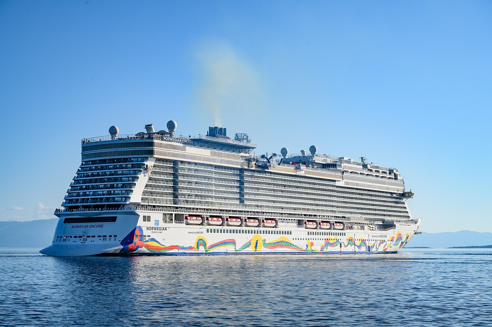 Norwegian Encore with her rainbow hull artwork sailing on flat blue water under a clear sky