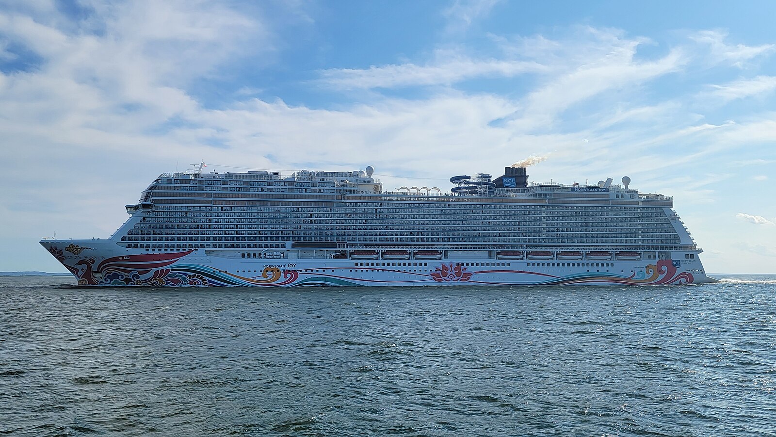 Norwegian Joy cruise ship under way at sea on a bright day with blue sky