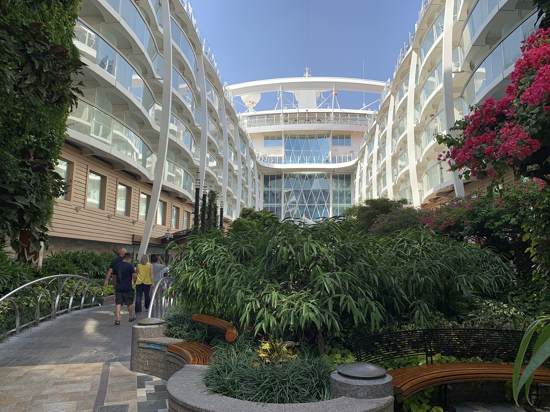 Leafy Central Park neighbourhood on Oasis of the Seas with pink bougainvillea, benches and balconies under a blue sky
