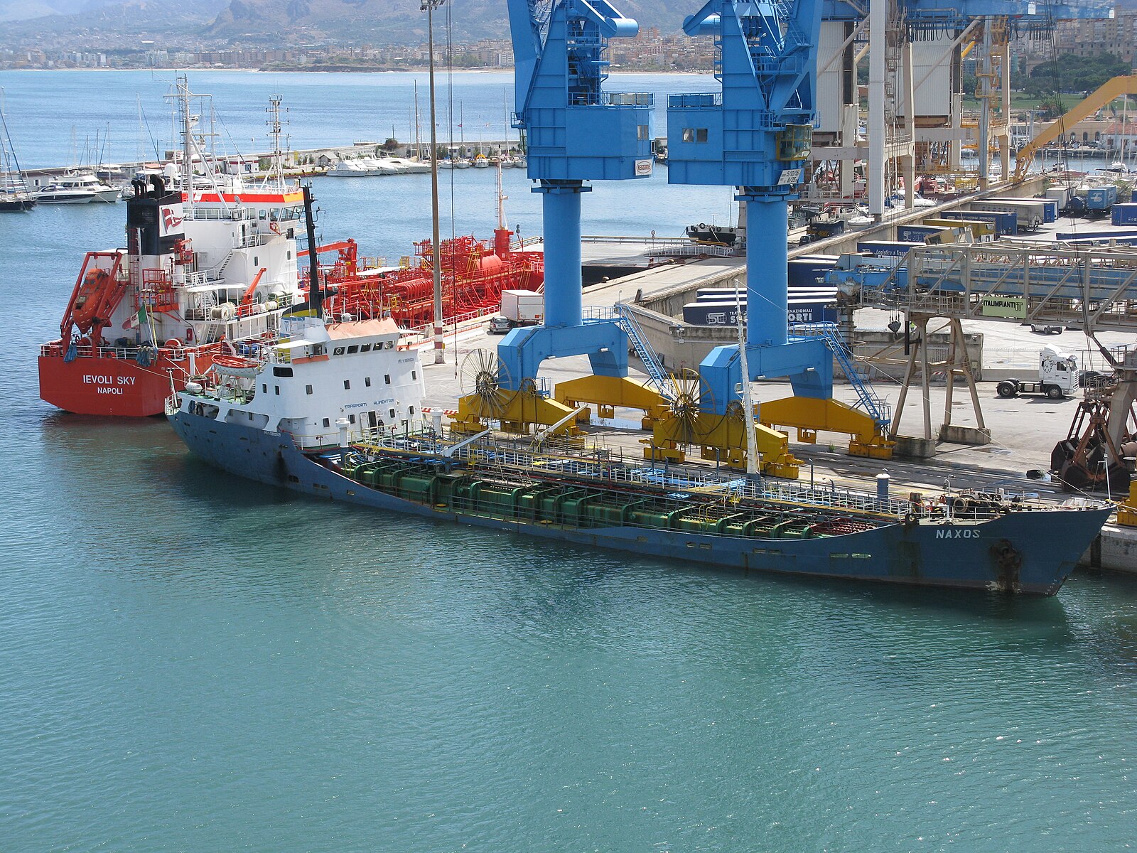 Ships moored beside blue cranes in the turquoise water of the port of Palermo, Sicily