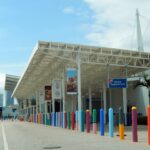 Covered check-in and baggage drop-off area at a PortMiami cruise terminal, lined with brightly painted bollards under a blue sky