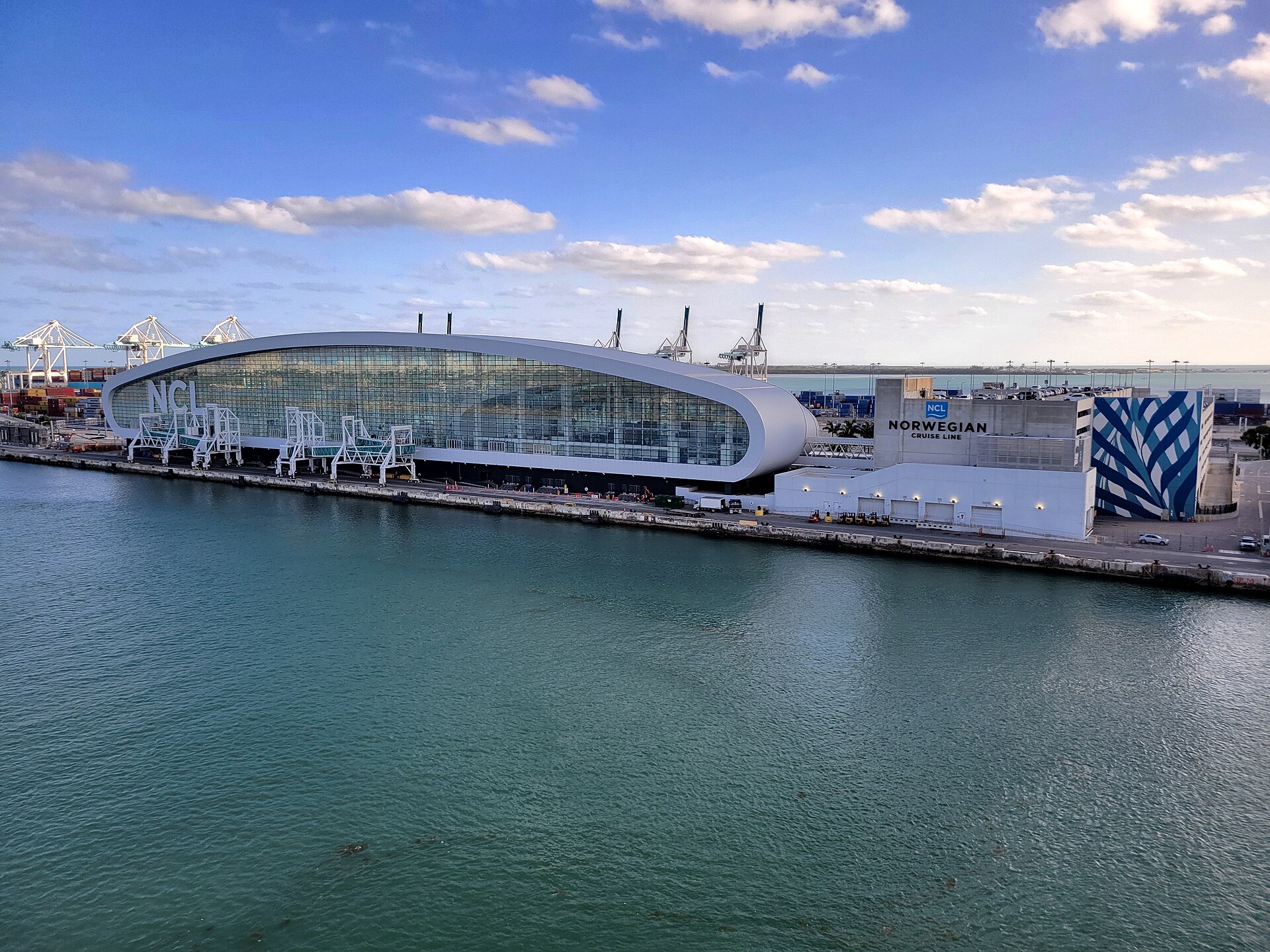 Norwegian Cruise Line's curved glass Terminal B at PortMiami under a blue sky