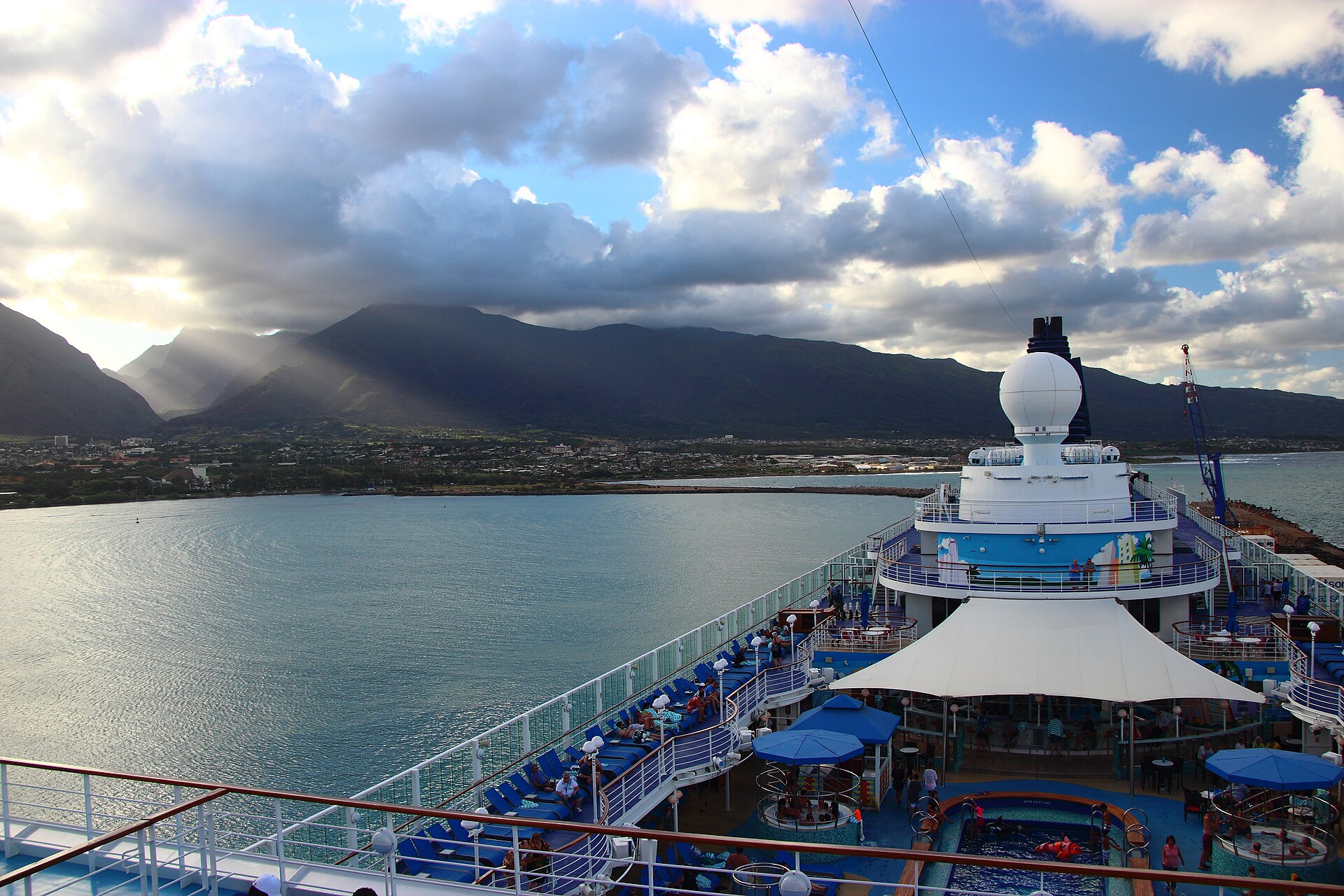 The blue pool deck of Norwegian's Pride of America looking out over Hilo Bay, Hawaii, with green mountains and clouds