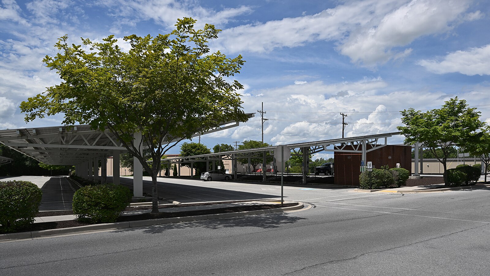 A parking lot shaded by a white solar canopy under a bright blue sky with green trees