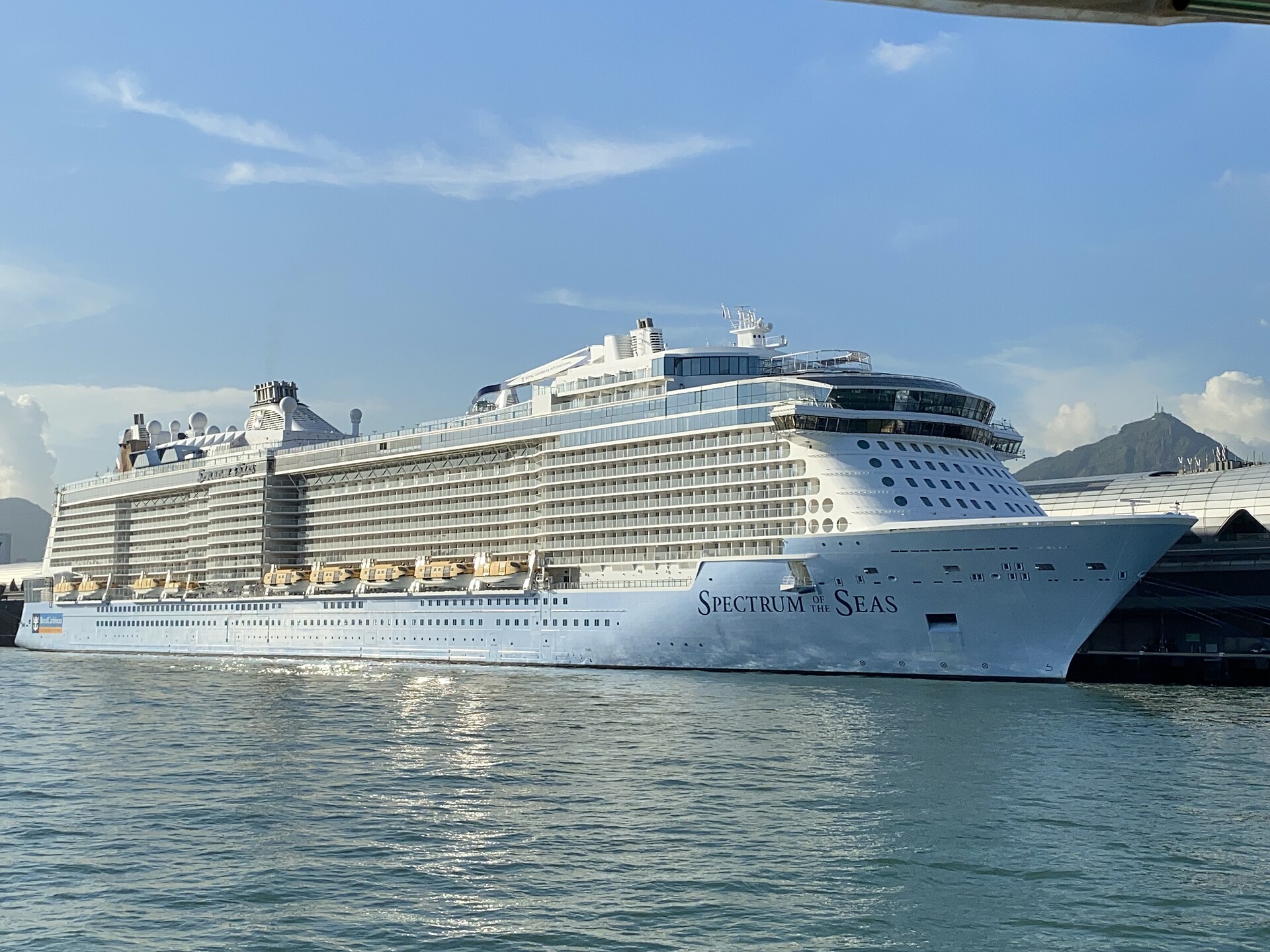 Royal Caribbean cruise ship Spectrum of the Seas alongside a terminal with green hills and a blue sky