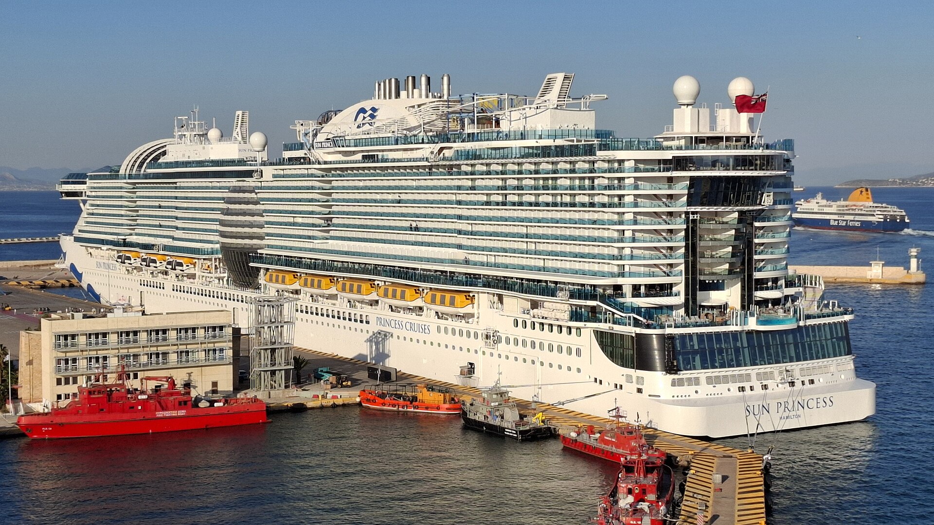 Princess Cruises ship Sun Princess docked at Piraeus, Greece, with red tugboats in the blue harbour