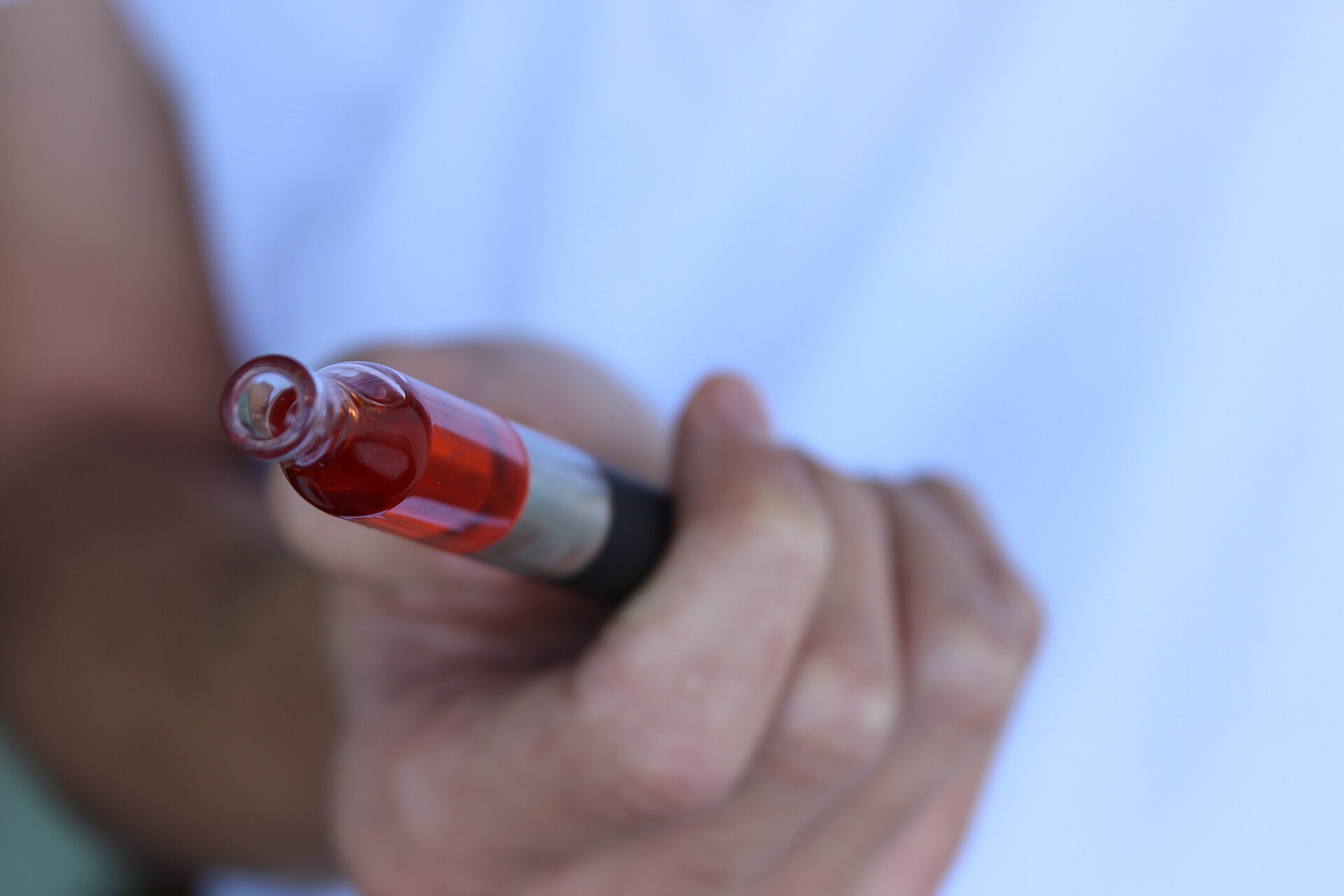 Hand holding a vape pen with a clear tank of red e-liquid
