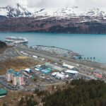 Aerial view of Whittier, Alaska, with a cruise ship alongside the waterfront and snow-covered mountains across Passage Canal