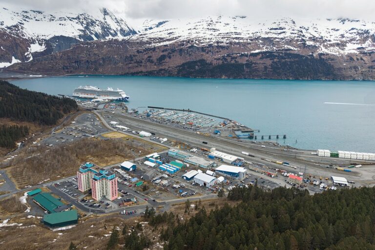 Aerial view of Whittier, Alaska, with a cruise ship alongside the waterfront and snow-covered mountains across Passage Canal