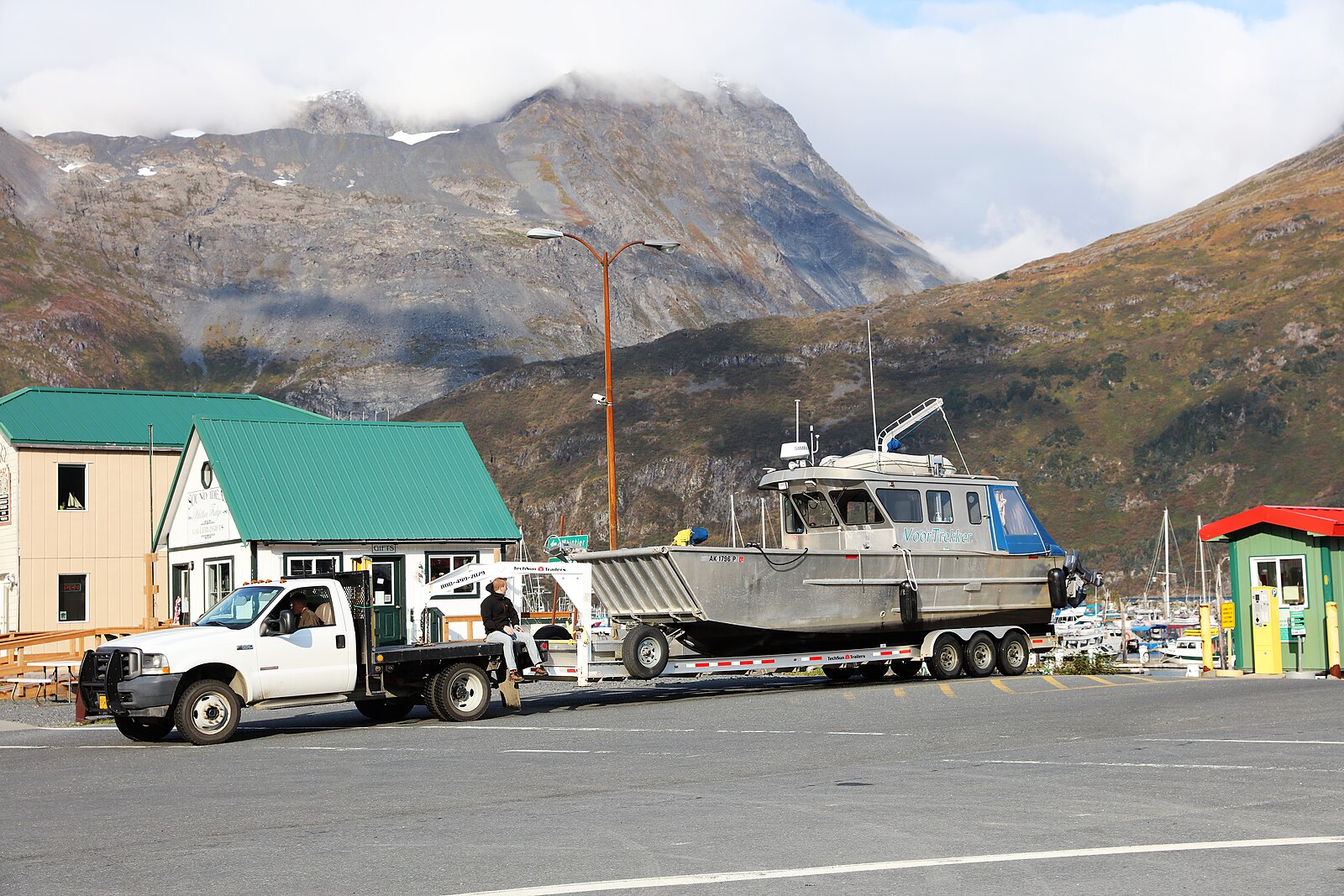 Whittier, Alaska waterfront in September with green-roofed buildings, a boat on a trailer and mountains behind