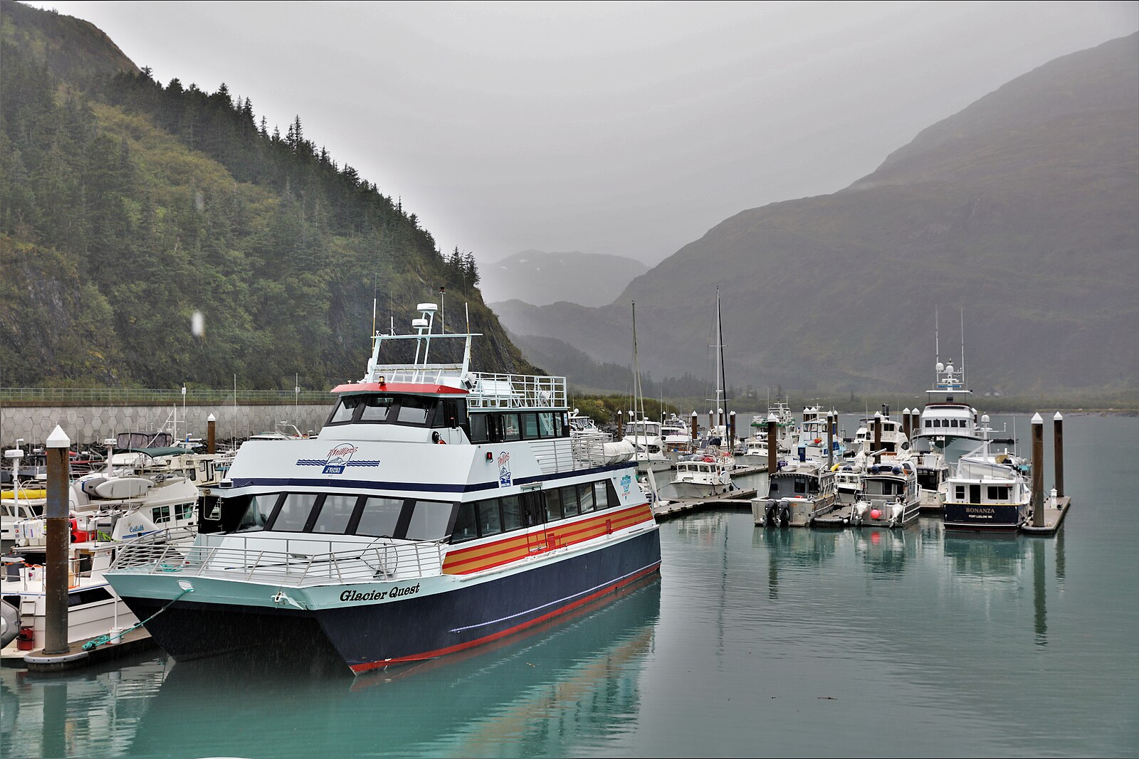 A blue and orange day-tour catamaran moored in Whittier's small-boat harbour in Alaska
