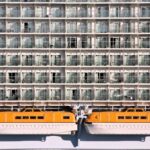 Rows of balcony cabins on the side of Allure of the Seas, with bright orange lifeboats hanging below the lowest row