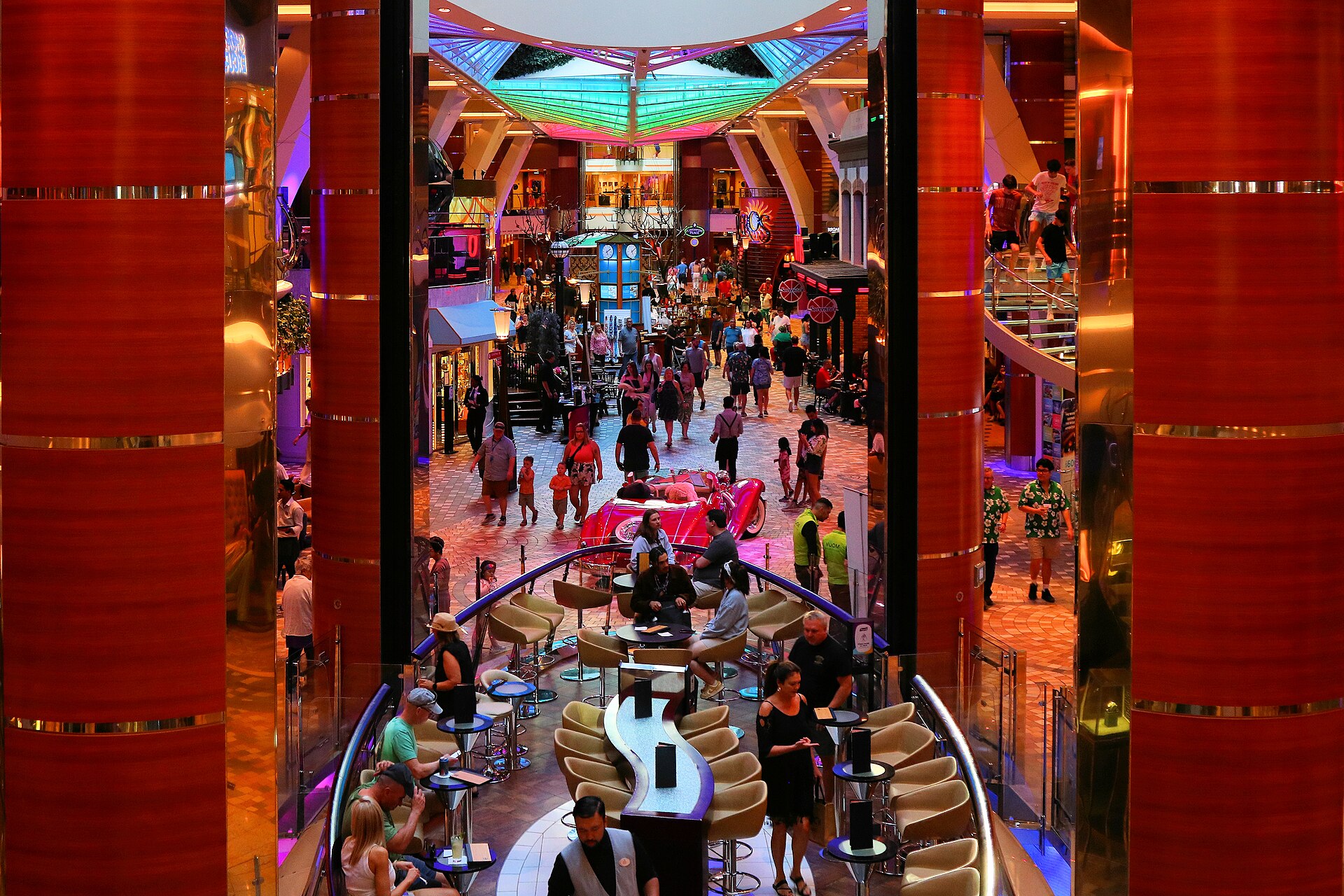 Crowds, shops, a bar and a red classic car on the brightly lit Royal Promenade of Allure of the Seas