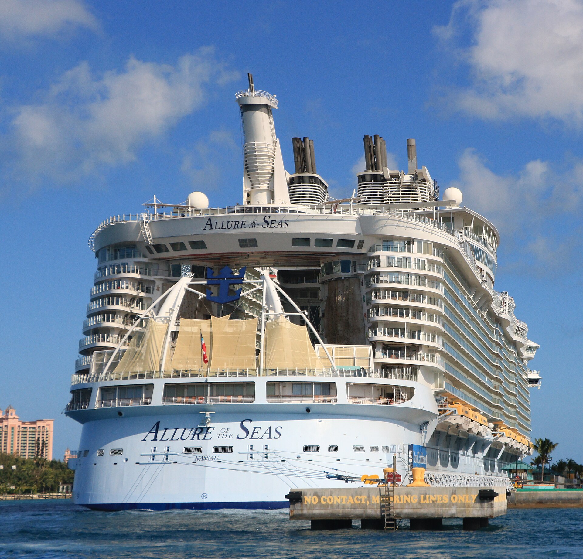 The stern of Allure of the Seas in Nassau under a blue sky, with tiers of curved aft-facing balconies above the AquaTheater