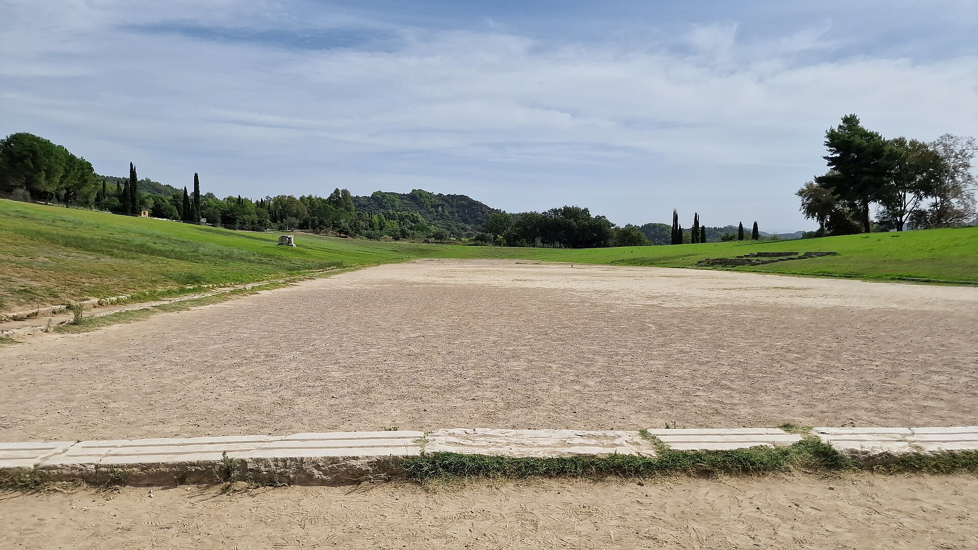 The ancient stadium at Olympia, Greece: a long dirt running track between green grass banks, with the stone starting line in front