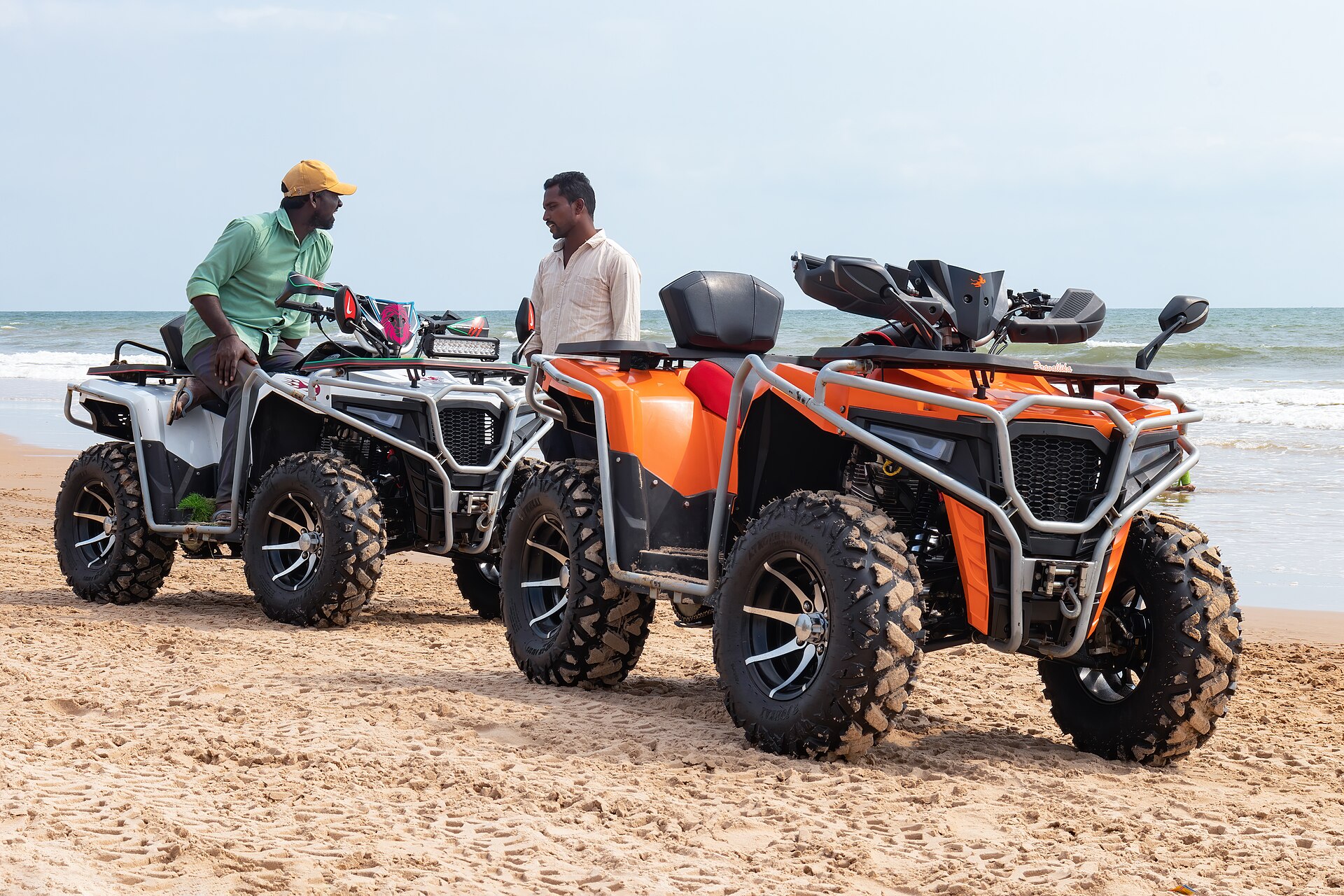 Two all-terrain vehicles, one orange and one white, parked on a sandy beach