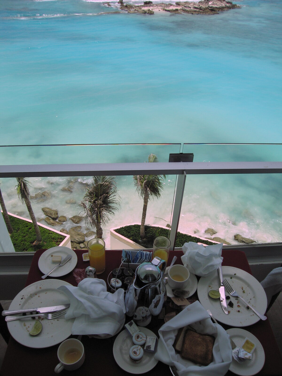 A finished breakfast for two on a balcony table above turquoise Caribbean water and palm trees