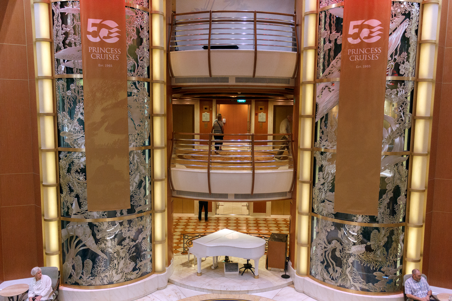Atrium of Caribbean Princess with a white grand piano and Princess Cruises 50th anniversary banners