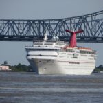 Carnival Elation with its red winged funnel sailing down the Mississippi River away from the Port of New Orleans, with the Crescent City Connection bridge behind