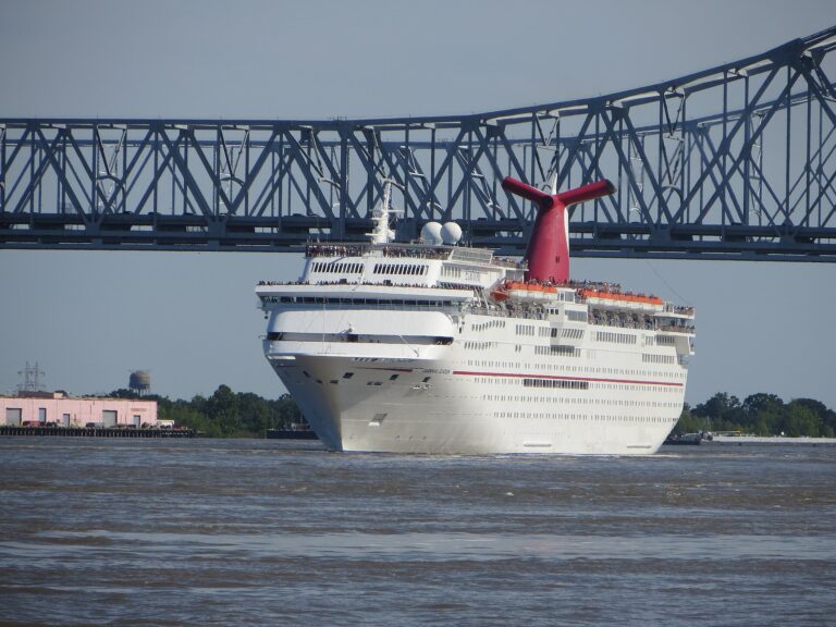 Carnival Elation with its red winged funnel sailing down the Mississippi River away from the Port of New Orleans, with the Crescent City Connection bridge behind