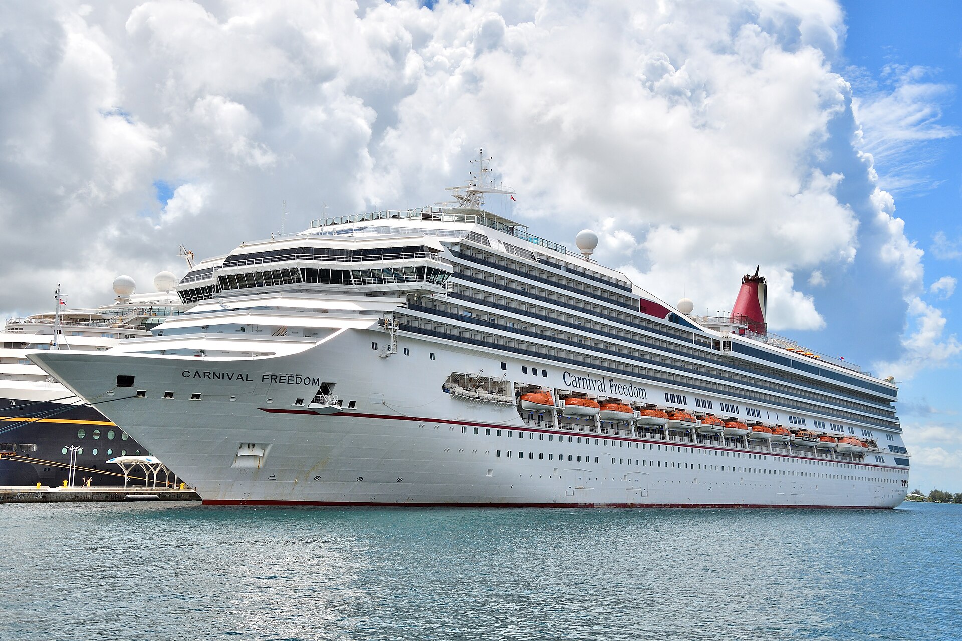 Carnival Freedom docked under blue sky and white clouds, with a short straight red funnel instead of the whale tail