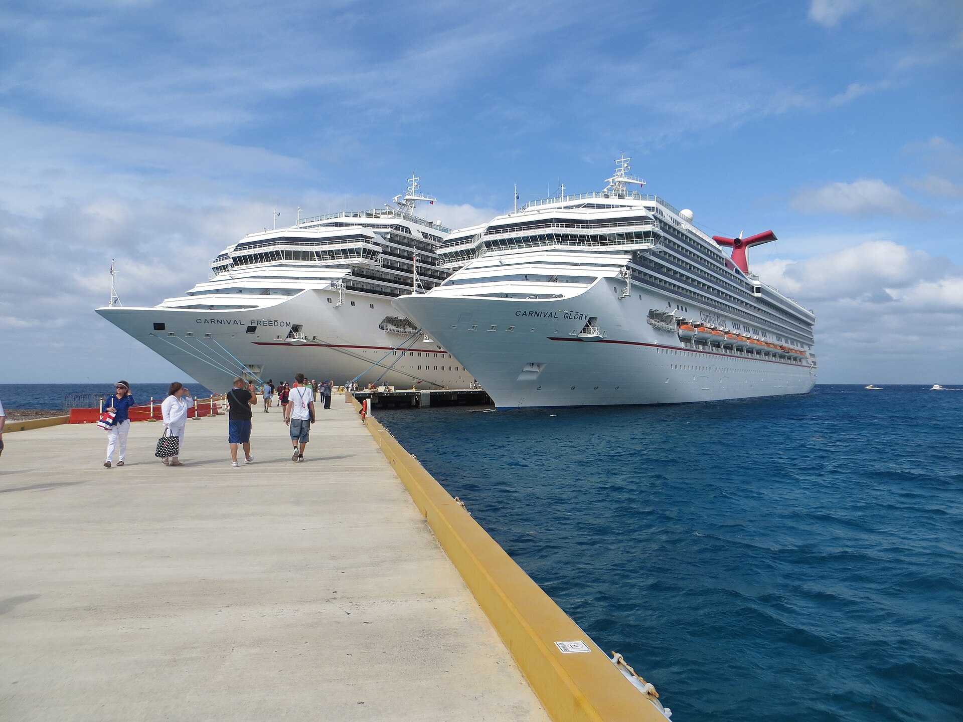 Passengers walking along the Cozumel pier beside Carnival Freedom and Carnival Glory on a sunny day
