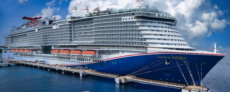 Carnival Jubilee docked at a pier in Cozumel under a bright blue sky, passengers walking ashore