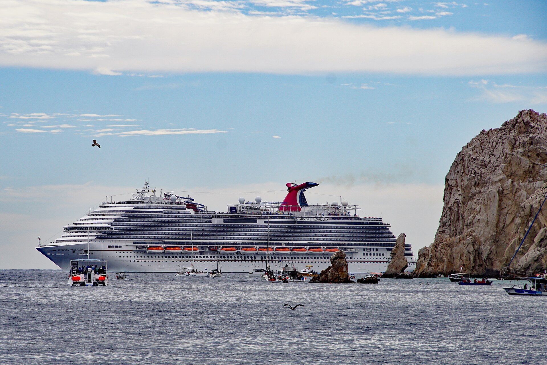 Carnival Panorama anchored off Cabo San Lucas with small boats and rocks in the foreground