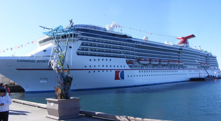 Carnival Spirit cruise ship docked beside a waterfront promenade under a clear blue sky